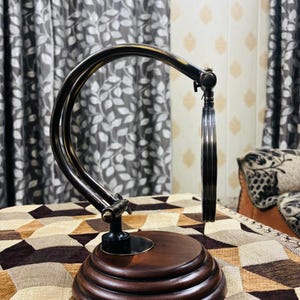 May include: A vintage-style magnifying glass with a dark brown wooden base and a silver-toned adjustable arm. The magnifying glass is circular and has a clear lens.