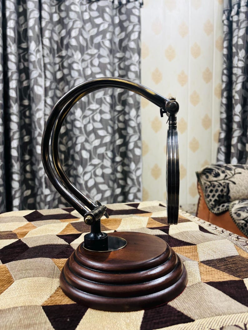 May include: A vintage-style magnifying glass with a dark brown wooden base and a silver-toned adjustable arm. The magnifying glass is circular and has a clear lens.
