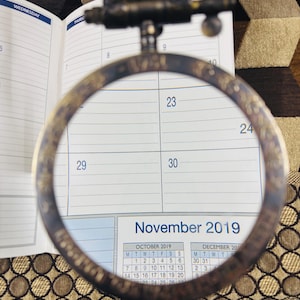 May include: A close-up of a calendar page with a magnifying glass over the dates 23, 24, 29, and 30. The calendar shows the months of October and December 2019, with November 2019 highlighted.