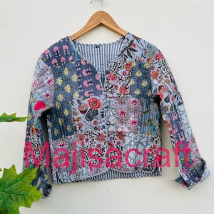 May include: A patchwork jacket with a V-neck and long sleeves. The jacket features a variety of floral patterns in shades of blue, pink, and white. The text "majiscraft" is visible on the front. The jacket is hanging on a wooden hanger.