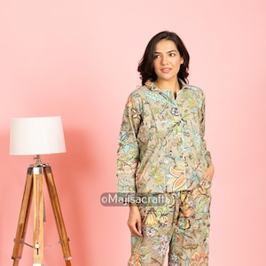 Puede incluir: Conjunto de pijama beige con estampado floral. La parte superior de manga larga tiene botones y cuello. Los pantalones son rectos. El estampado floral incluye naranja, verde y azul. El texto "Majisacraft" es visible.