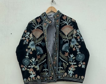 Könnte beinhalten: Schwarz bestickte Jacke mit Blumen- und Blattmotiven in Blau-, Pfirsich- und Grüntönen. Die Jacke hat einen Stehkragen und ein gestreiftes Futter. Die Jacke hängt an einem Holzbügel.