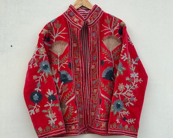 Könnte beinhalten: Rote Jacke mit aufwendiger Blumenstickerei in Blau-, Gold- und Grüntönen. Die Jacke hängt an einem Holzbügel vor weißem Hintergrund. Die Stickerei ist detailliert und bedeckt Vorder- und Ärmel.