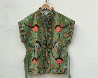 Può includere: Un gilet senza maniche verde oliva con ricami floreali intricati nei toni del corallo, blu e oro. Il gilet presenta un collo alto e lunghi lacci abbinati. La fodera interna ha un motivo a righe. Lunghezza di circa 50 cm.