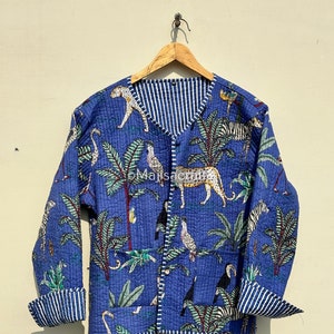 Puede incluir: Chaqueta acolchada azul con estampado de animales de la jungla, incluyendo leopardos, cebras y pájaros. La chaqueta tiene forro y puños a rayas. La chaqueta está colgada en una percha de madera.