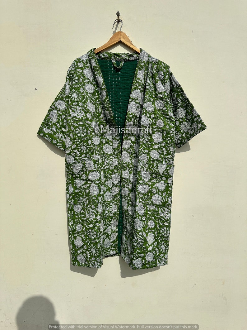 Może przedstawiać: Zielono-biała kurtka w stylu kimono z kwiatowym nadrukiem, wisząca na drewnianym wieszaku. Kurtka ma kr&oacute;tkie rękawy i ciemnozieloną podszewkę. Na ubraniu widoczny jest napis "Majisacraft".