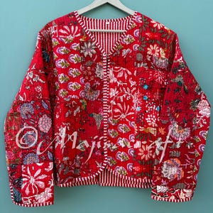 May include: A red floral print jacket with a striped trim and lining. The jacket features a V-neck and long sleeves. The floral pattern includes various colors and shapes. The jacket is hanging on a white hanger.