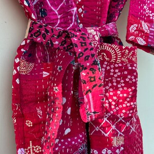 Pode incluir: Robe de patchwork em tons de vermelho e rosa, com v&aacute;rios padr&otilde;es florais e geom&eacute;tricos. O robe tem um cinto a condizer com um design de padr&atilde;o de leopardo. As costuras brancas detalham as costuras e os padr&otilde;es, criando um visual texturizado.