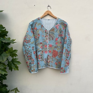 May include: A reversible quilted jacket with a floral design in red, pink, and yellow on a light blue base. The jacket has a V-neck and long sleeves. The reverse side has a blue and white striped pattern.