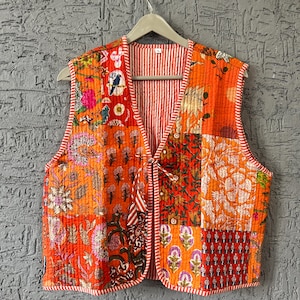 Puede incluir: Un chaleco patchwork en tonos naranja, rojo y rosa, con estampados florales y geométricos. El chaleco tiene cuello en V, cierre de lazo y forro a rayas. Los bordes están ribeteados con tela a rayas rojas y blancas.