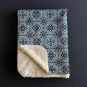 May include: A black and white patterned baby blanket with a soft, beige fleece lining.