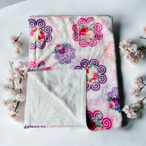 May include: A soft, white and pink fleece blanket with a floral pattern. The blanket has a white fleece backing.