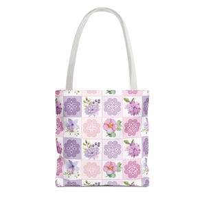 May include: A white tote bag with a purple and pink floral pattern. The pattern features a repeating design of flowers and swirls.