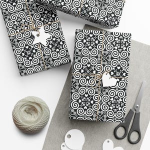 May include: Three black and white gift boxes wrapped in paper with a swirling pattern. The boxes are tied with twine and have white paper stars and hearts attached.