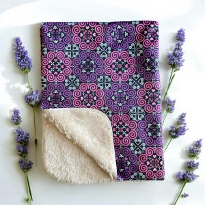 May include: A soft, pink and purple patterned baby blanket with a white fleece backing. The blanket features a repeating pattern of hearts and swirls.