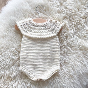 May include: A white crocheted baby onesie with a lacy collar and button closures.