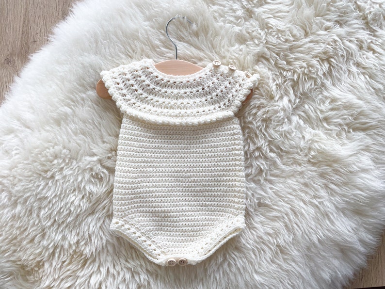 May include: A white crocheted baby onesie with a lacy collar and button closures.