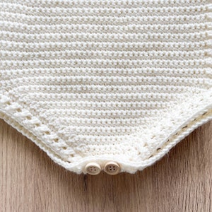 May include: A white crocheted baby onesie with a scalloped edge and two wooden buttons.