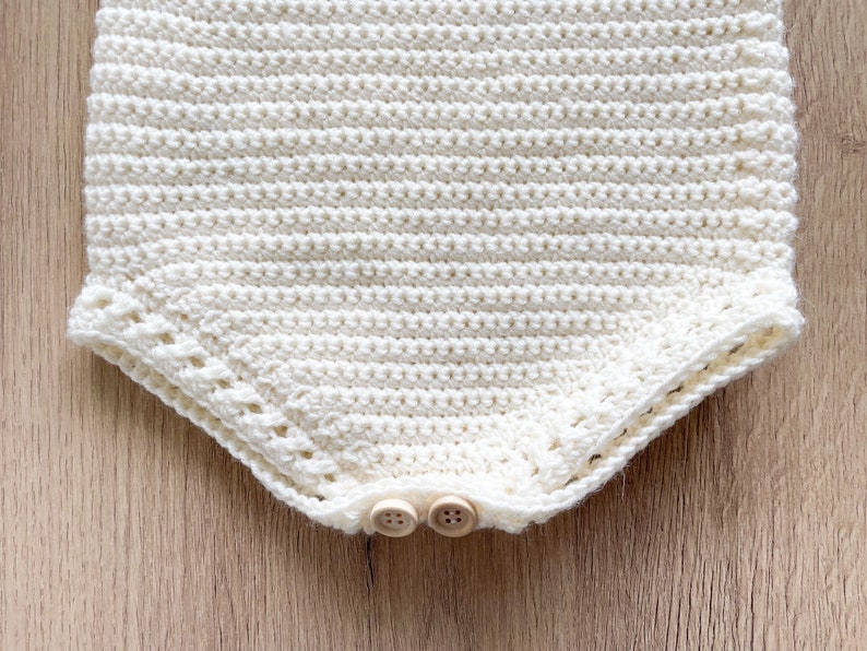 May include: A white crocheted baby onesie with a scalloped edge and two wooden buttons.