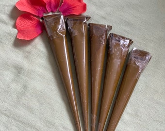 May include: Five brown henna cones with plastic tips, arranged in a fan shape on a light green fabric background.  A cluster of red flower petals are at the top of the image.