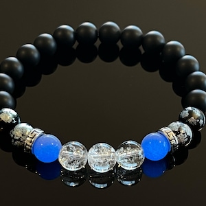 Op de afbeelding: Een kralenarmband met matte zwarte onyx kralen, afgewisseld met blauwe en heldere kristallen kralen. De armband heeft zilverkleurige metalen accenten en is ontworpen om om de pols te dragen.