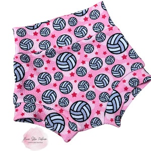 May include: Pink high-waisted shorts with a repeating pattern of volleyballs and red stars. The volleyballs are white and light blue with black outlines. The shorts have a textured fabric and a high waistband.