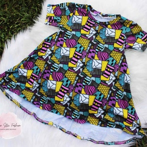 Könnte beinhalten: Ein farbenfrohes Patchwork-Kleid mit einem schwarzen, weißen, gelben, blauen, rosa und violetten Muster. Das Kleid hat kurze Ärmel und einen runden Ausschnitt. Das Kleid ist aus einem weichen, dehnbaren Stoff.  "Pixie Stix Fashion - Fashion Sweet Boutique"