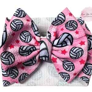 May include: A large pink hair bow with a volleyball pattern and red stars. The bow is tied in the center and has a white headband. The text "Pixie Stix Fashion" is in the upper right corner.
