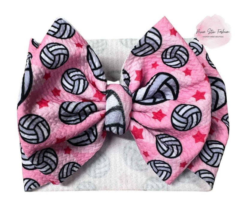May include: A large pink hair bow with a volleyball pattern and red stars. The bow is tied in the center and has a white headband. The text "Pixie Stix Fashion" is in the upper right corner.