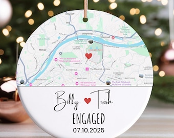 May include: A white ceramic ornament with a map design and the words "Billy ❤️ Trish ENGAGED 07.10.2025." The top half features a map with a red heart. A gold string is attached for hanging.