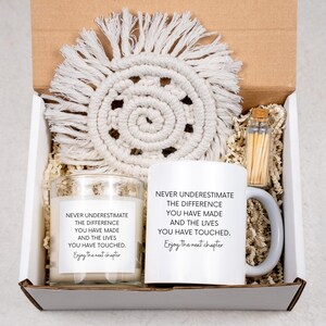 May include: A gift box containing a white ceramic mug and a glass candle, both with the text "Never underestimate the difference you have made and the lives you have touched. Enjoy the next chapter." Also included is a macrame coaster and a small glass bottle of matches.