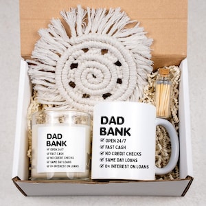 May include: A gift box containing a white ceramic mug and a glass candle, both labeled "DAD BANK" with a list of services. A macrame coaster and a small glass bottle of matches are also included.
