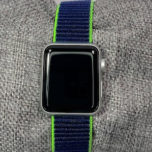 May include: A silver Apple Watch with a black screen and a blue and green striped sport band.