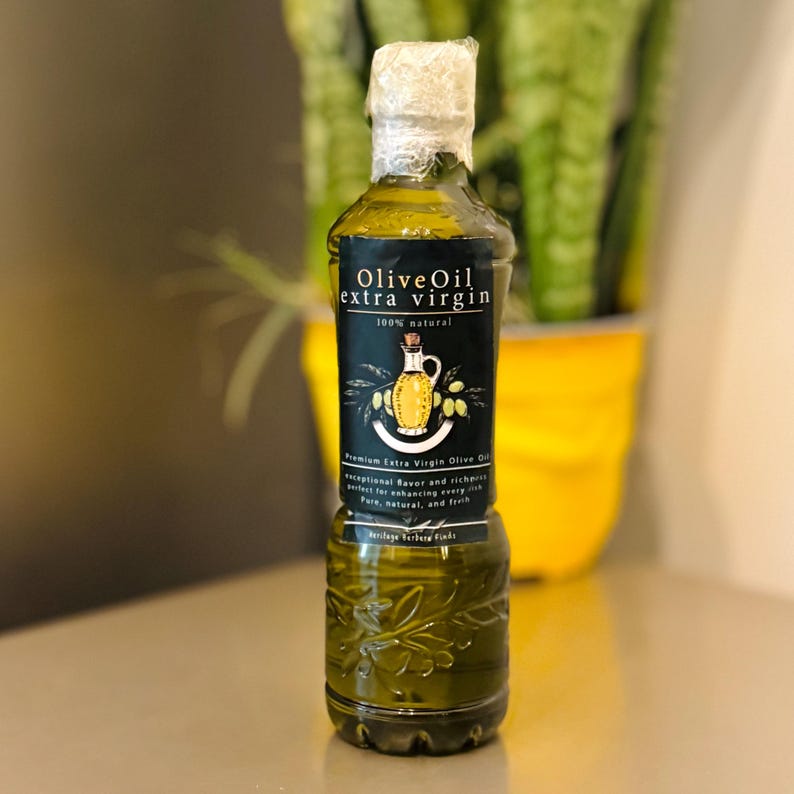 May include: A glass bottle of olive oil with a black label that reads "Olive Oil extra virgin 100% natural". The label also features a drawing of a jug of olive oil and olives.