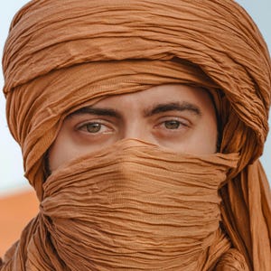 May include: A person wearing a brown headscarf that covers their face. The scarf is made of a soft, flowing fabric and is draped over the person's head and face.