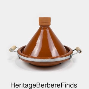 Peut inclure: Un tajine en céramique marron avec un couvercle conique et une base ronde. Le pot a un bord en métal et des poignées en bois. Le texte "HeritageBerbereFinds" est au bas de l'image.
