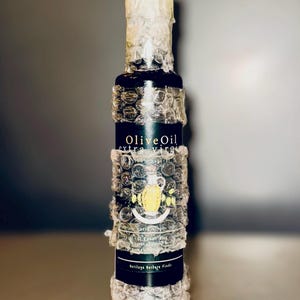 May include: A glass bottle of extra virgin olive oil wrapped in bubble wrap. The label reads "Olive Oil extra virgin" and "Heritage Berber Fields".