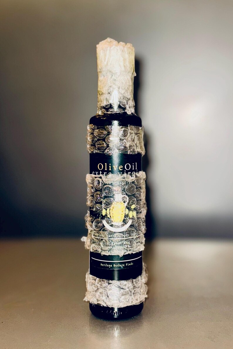 May include: A glass bottle of extra virgin olive oil wrapped in bubble wrap. The label reads "Olive Oil extra virgin" and "Heritage Berber Fields".