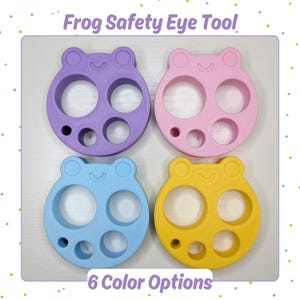 May include: Four frog-shaped safety eye tools in purple, pink, light blue, and yellow. Each tool features a frog face design with two large circular cutouts and two smaller circular cutouts. The text Frog Safety Eye Tool and 6 Color Options is visible.