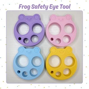 May include: Four colorful frog-shaped safety eye tools in purple, pink, blue, and yellow. Each tool has a circular design with three holes and a small eye-shaped hole. The text "Frog Safety Eye Tool" is at the top.