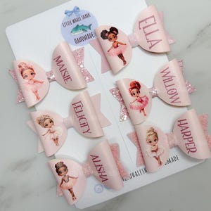 May include: Pink and white hair bows with a ballerina design and personalised names. The names are: Maisie, Ella, Willow, Harper, Felicity, Alisha.