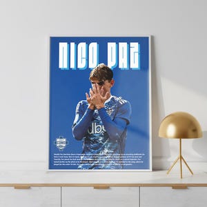 May include: A framed poster featuring the name "NICO PAZ" in large, white and blue block letters. The poster displays a soccer player in a blue jersey with his hands covering his face. The background is a solid blue.