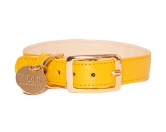 Puede incluir: Un collar para mascota de color amarillo brillante con superficie texturizada y forro interior color crema. El collar cuenta con una hebilla de metal dorado pulido y una etiqueta redonda de metal a juego grabada con el texto WOOF HANDMADE.