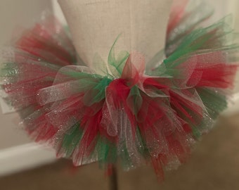 May include: A red, green, and white tulle tutu with silver glitter. The tutu is on a white dress form.