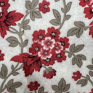 May include: Close-up of a fabric with a floral pattern. The design features clusters of red flowers with white centers and dark red leaves and stems against a light beige background. The fabric has a textured appearance.