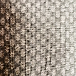 May include: Close-up of a textured fabric with a repeating pattern of white polka dots on a dark gray background. The fabric has a woven appearance, with visible threads creating a subtle grid.