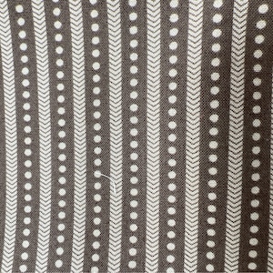 May include: Close-up of a fabric with a repeating pattern. The design features vertical stripes of white dots and chevron shapes against a dark brown background. The fabric has a textured appearance.