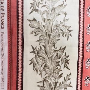 May include: Close-up of fabric with a repeating floral pattern in brown and cream. Vertical stripes in red and burgundy border the design. Text on the left side reads "ATELIER DE FRANCE French General 20th Anniversary 1997-2017 by Fré..."