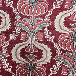May include: Close-up of a red fabric with a repeating floral pattern. The design features large, stylized flowers in shades of red and pink, with accents of green and beige. The background is a deep red.