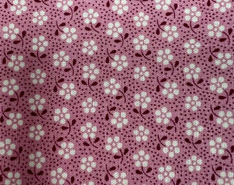 May include: Close-up of a pink fabric with a repeating floral pattern. The flowers are white with dark red stems and leaves. The background is a solid pink color with a subtle dotted texture, creating a vintage or cottagecore aesthetic.